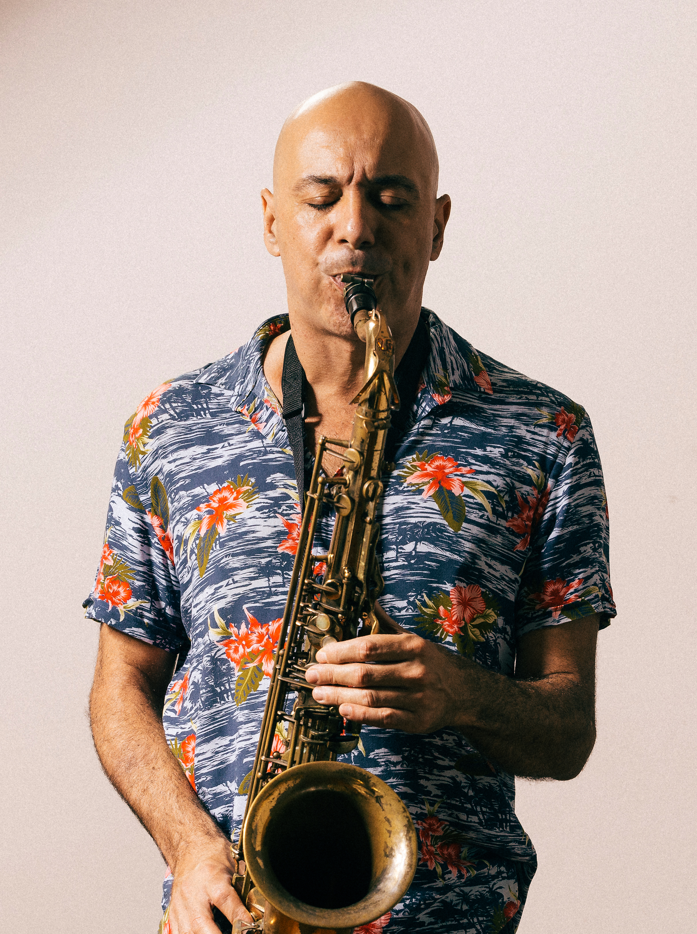 Marcelo Monteiro, homem branco, olhos escuros e estatura media, tocando sax com blusa de botão de flores